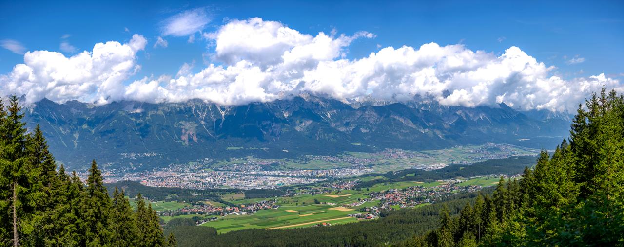 Panoramablick auf eine Stadt vor majestätischen, wolkenverhangenen Alpen im blauen Himmel