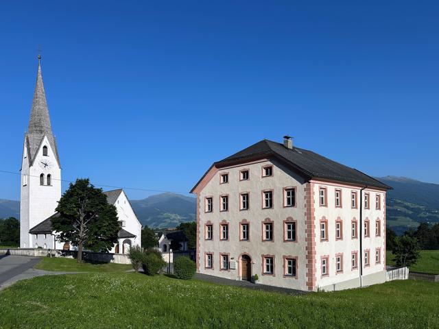 Historische Szenerie mit einer Kirche und einem traditionellen Gebäude in ländlicher Umgebung